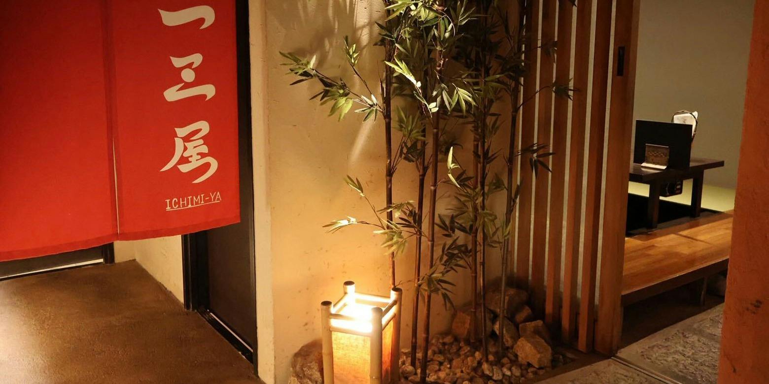 赤い暖簾に白い筆文字の「一三屋」。竹と行灯が照らす入口